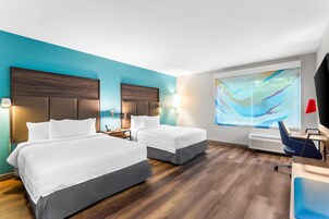 Habitación de hotel con dos camas, un escritorio y un ventanal con vistas.