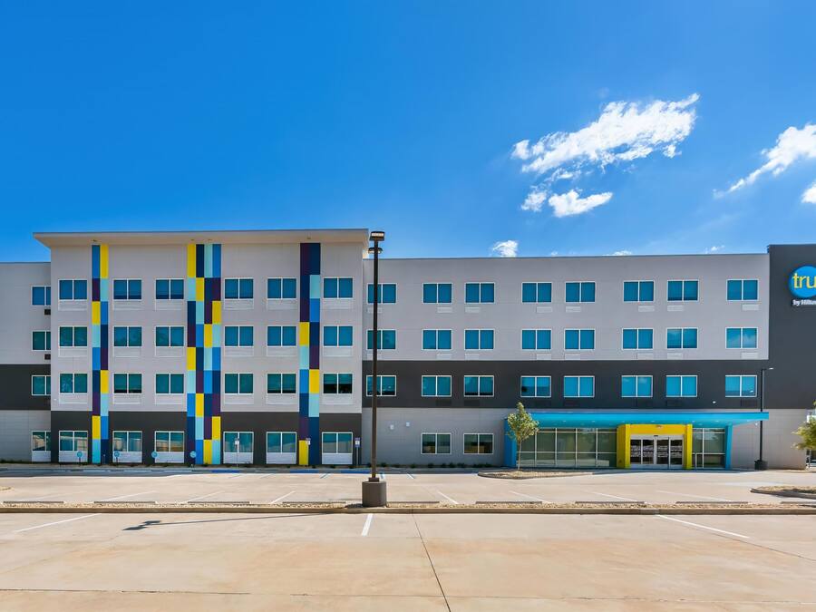 A modern hotel building with a multi-story structure, a prominent logo, and a parking lot in front.