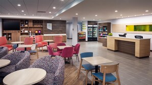 Un moderno vestíbulo de hotel con zonas de estar, un mostrador de recepción y una estación de bebidas de autoservicio.