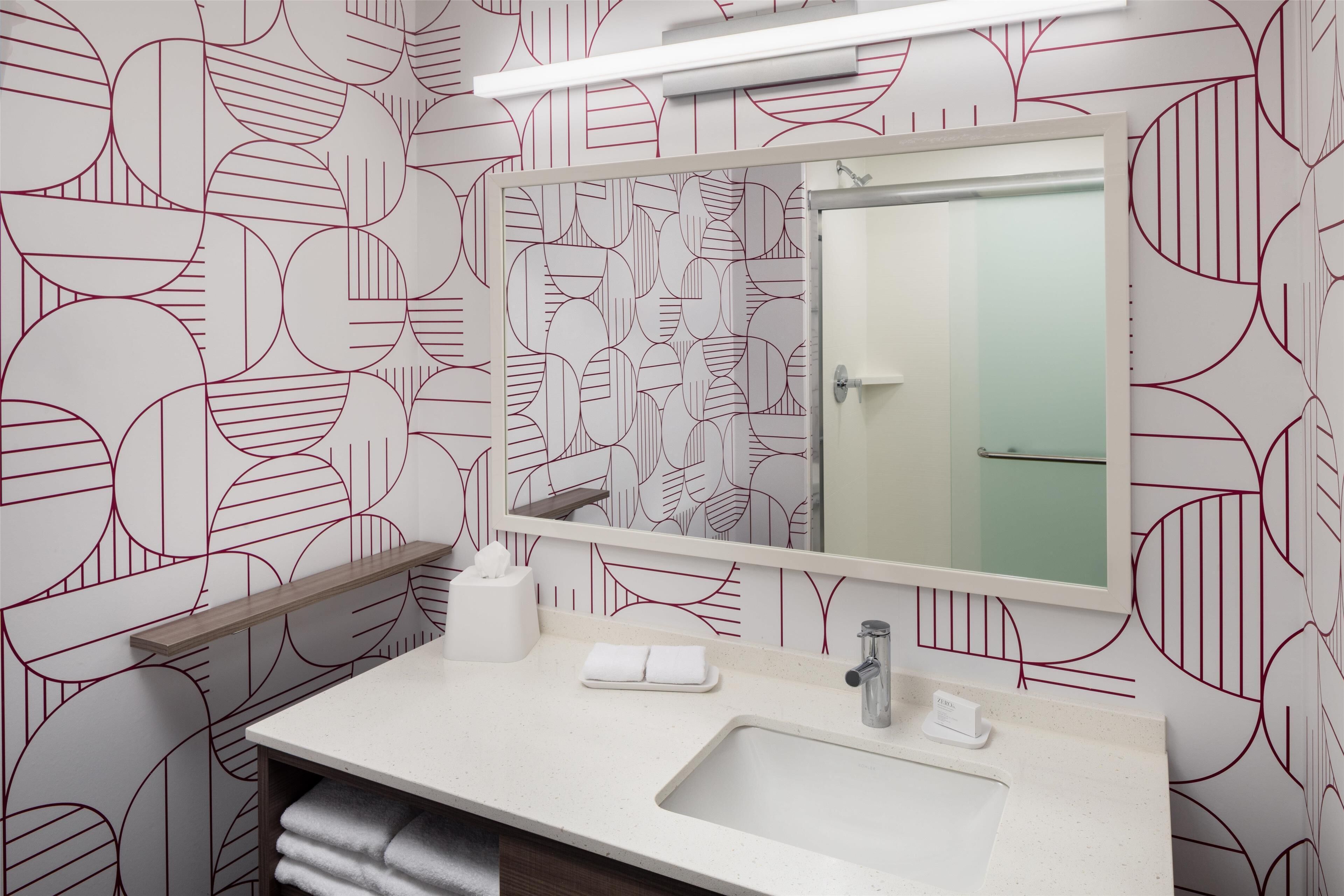 A bathroom with a geometric patterned wallpaper, a white sink, a mirror, and a towel rack.