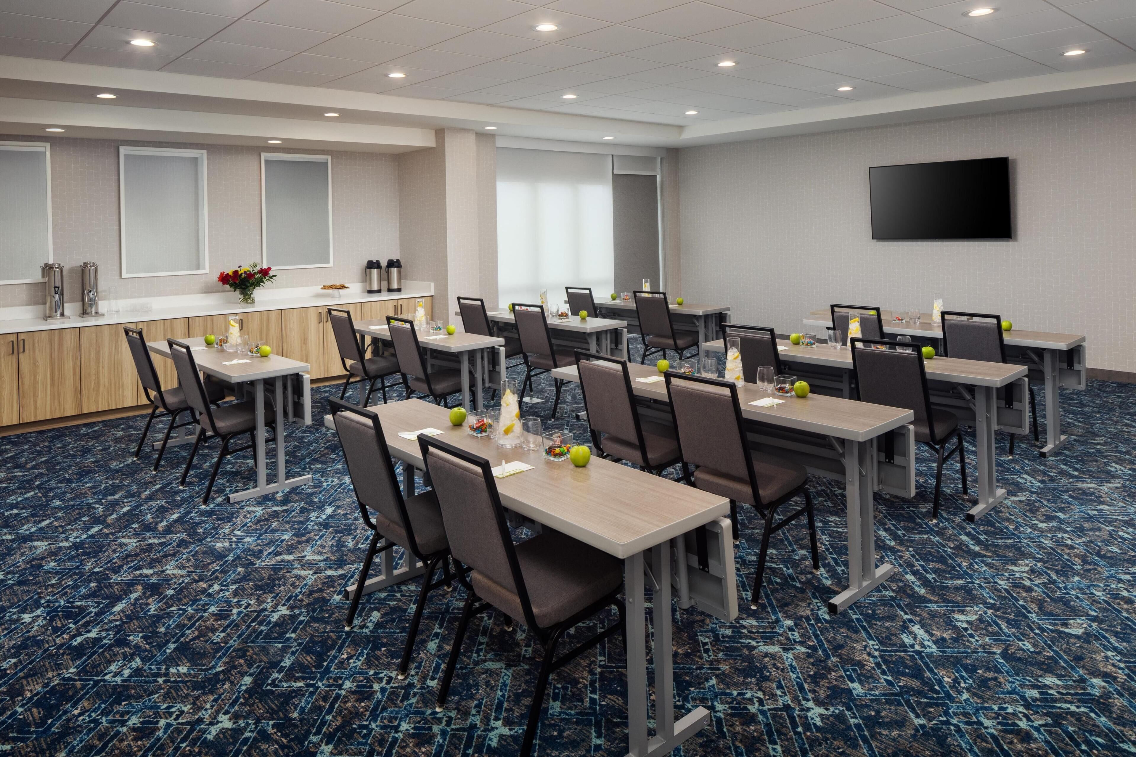 A conference room with multiple tables and chairs, a counter with a vase of flowers, and a flat-screen TV on the wall.