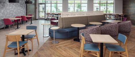 A modern cafe with round tables, blue and red chairs, and a blue sofa area.