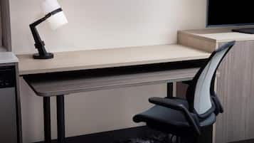 Un escritorio moderno con una lámpara de escritorio negra, una silla de oficina negra y un monitor de computadora.