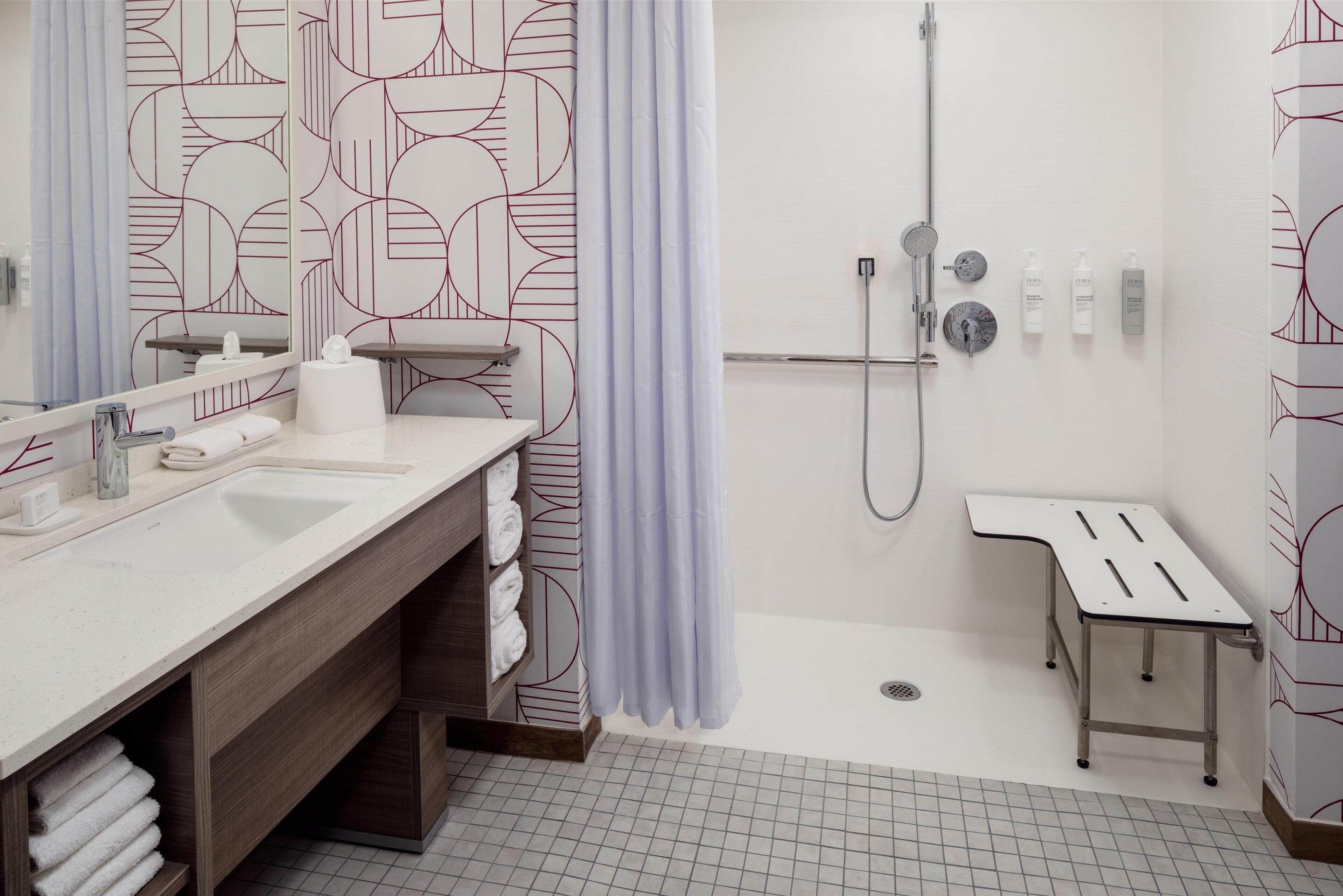 A modern bathroom with a large mirror, two sinks, a shower area, and a small table.