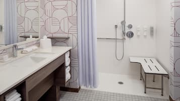 A modern bathroom with a large mirror, two sinks, a shower area, and a small table.