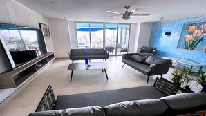 A modern living room with a large TV, two sofas, a coffee table, and a balcony with a city view. - Cozy Condo in Acapulco – Perfect for Long Stays & Work Trips (Acapulco de Juárez)
