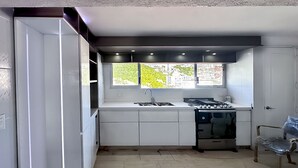 A modern kitchen with white cabinets, a built-in stove, and a window providing a view of greenery outside. - Cozy Condo in Acapulco – Perfect for Long Stays & Work Trips (Acapulco de Juárez)