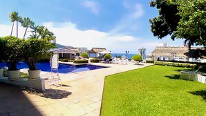 A pool area with lounge chairs, a small building, and a view of the ocean. - Cozy Condo in Acapulco – Perfect for Long Stays & Work Trips (Acapulco de Juárez)