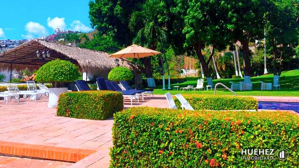 A well-maintained outdoor area with lounge chairs, a thatched-roof structure, and neatly trimmed hedges. - Cozy Condo in Acapulco – Perfect for Long Stays & Work Trips (Acapulco de Juárez)