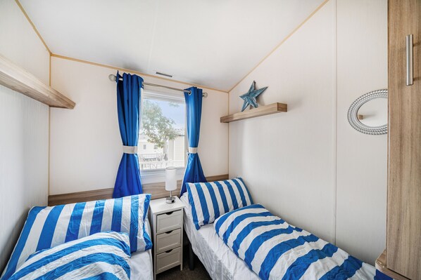 A bedroom with two single beds, a window with curtains, a star decoration, and a small table with a lamp. - 3 Bed-sleeps 8-pet Friendly-parking-sea View (Exmouth)