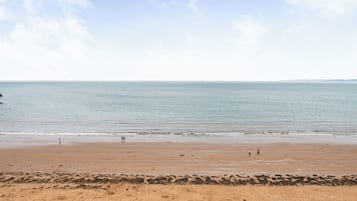 A wide sandy beach with gentle waves, a clear sky, and a distant shoreline.