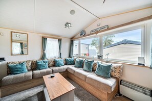 A cozy living room with a sectional sofa, a coffee table, and a large window with a view of a house. - 3 Bed-sleeps 8-pet Friendly-parking-sea View (Exmouth)