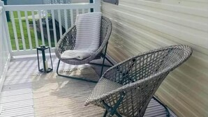 Een overdekt terras met rieten stoelen en een bijzettafeltje.