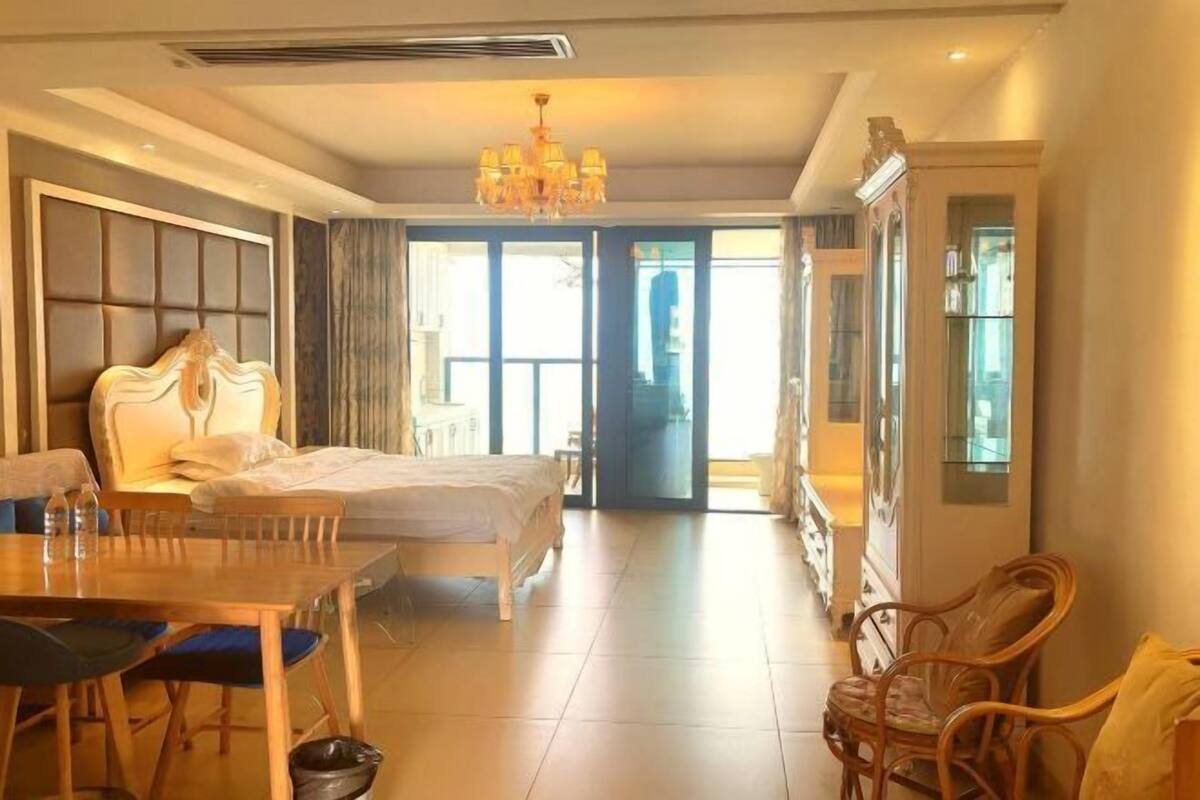 Ein Hotelzimmer mit einem großen Bett, einem Esstisch mit Stühlen, einer Chandelierleuchtre und Blick durch Glastüren.