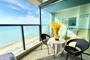Un balcon avec vue sur la mer, une petite table avec des chaises et une salle de bain avec un miroir et un lavabo.