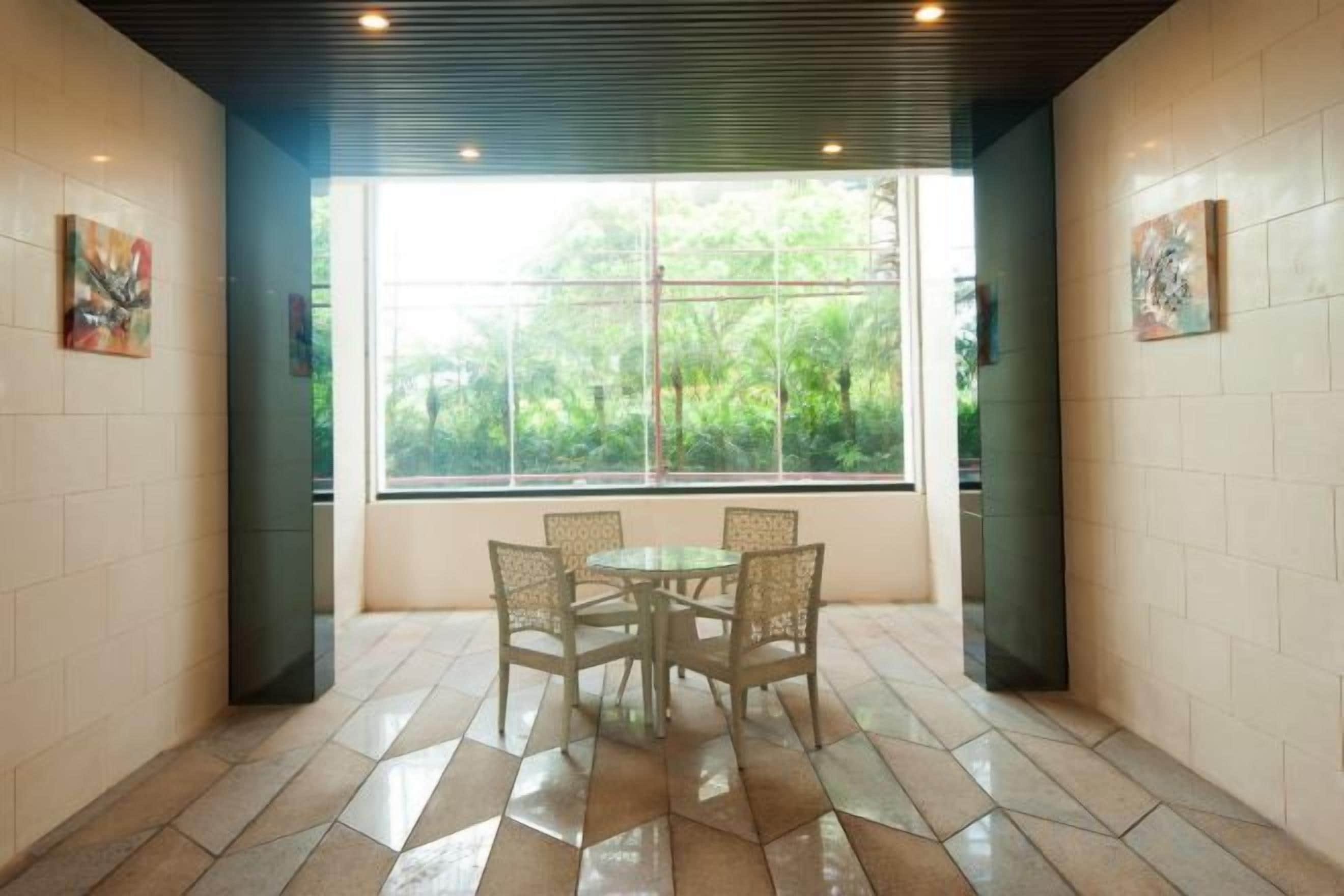 A dining area with a table and chairs, a window with a view of greenery, and tiled walls.