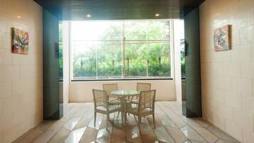 A dining area with a table and chairs, a window with a view of greenery, and tiled walls.