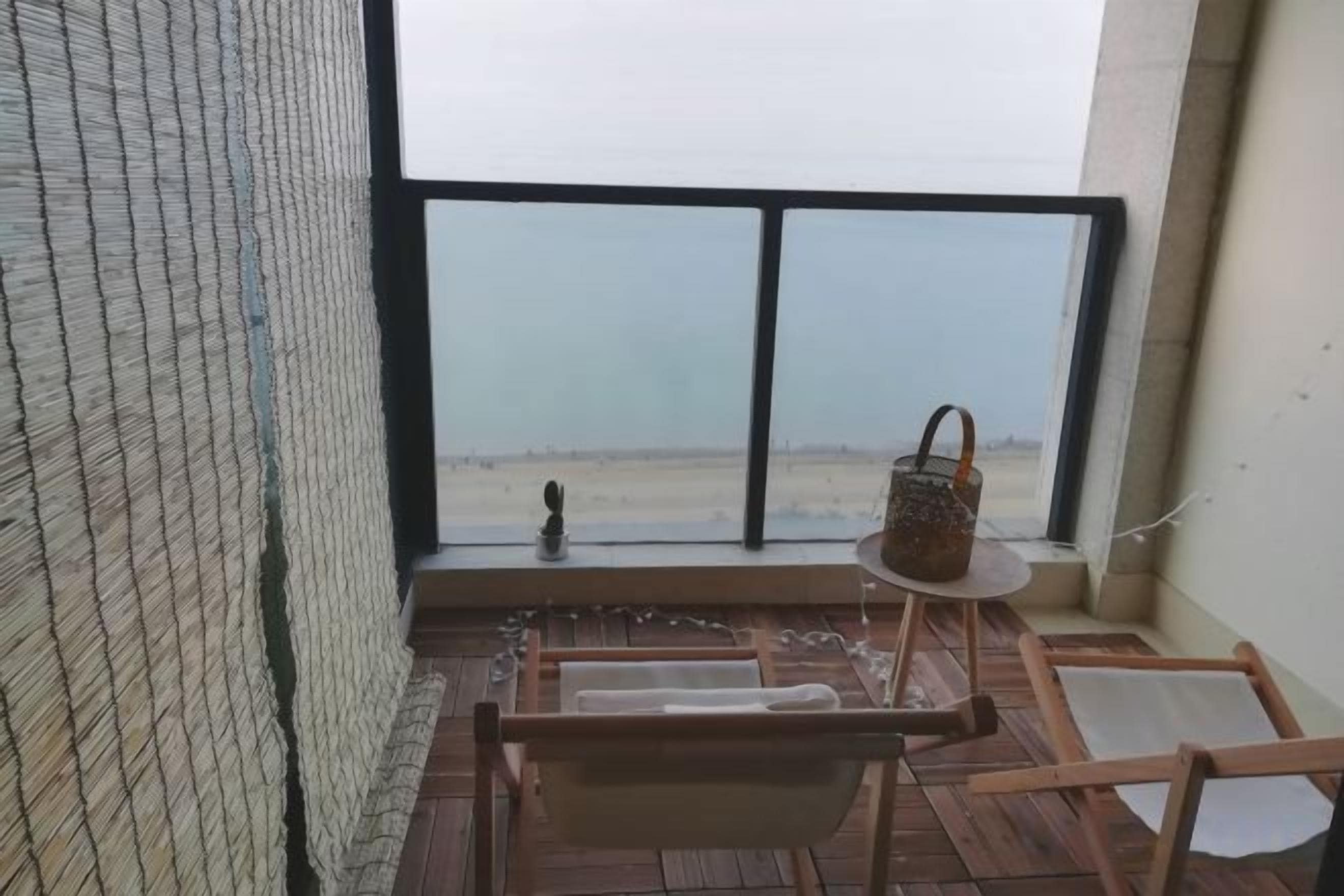 Ein Balkon mit Blick auf einen Strand, einer hängenden Blumenampel und einem Holzstuhl.