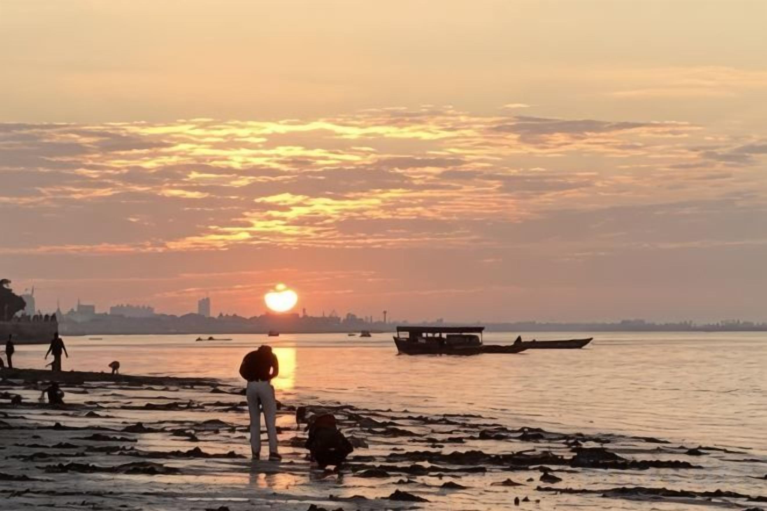 A sunset over a body of water with boats and people on the shore.