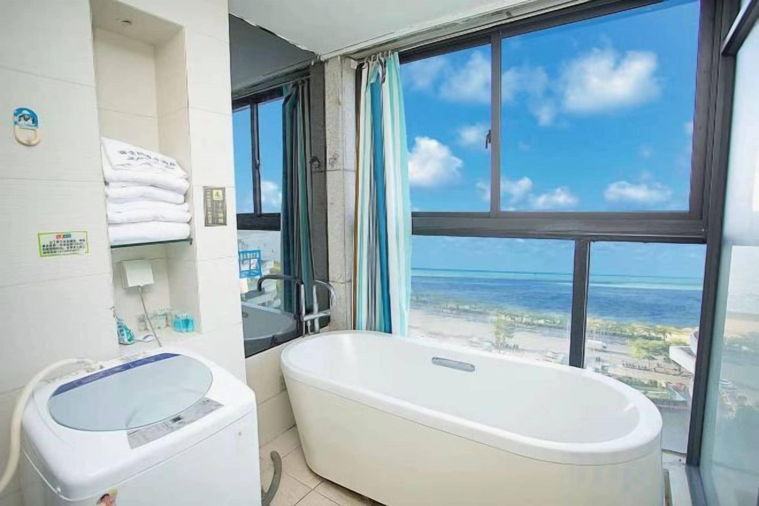 A bathroom with a bathtub, a sink, and a window with a view of the ocean.