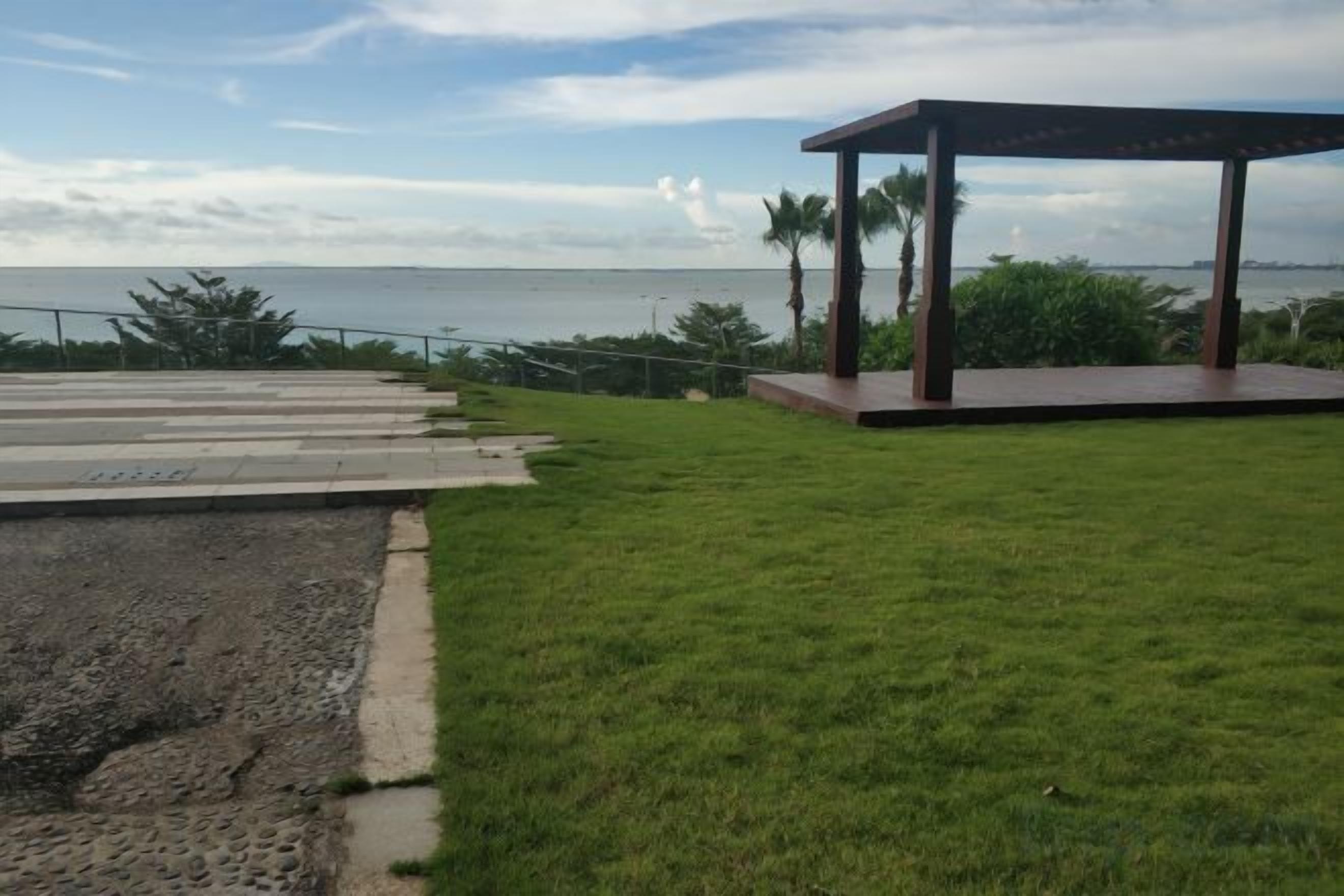 A grassy area with a wooden gazebo and a concrete pathway leading to a railing overlooking a body of water.