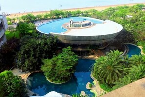 A circular pool with a central fountain, surrounded by lush greenery and a beach view. - Beibuwan Yihao Dibiao Seaview Apartment Hotel (Beihai)