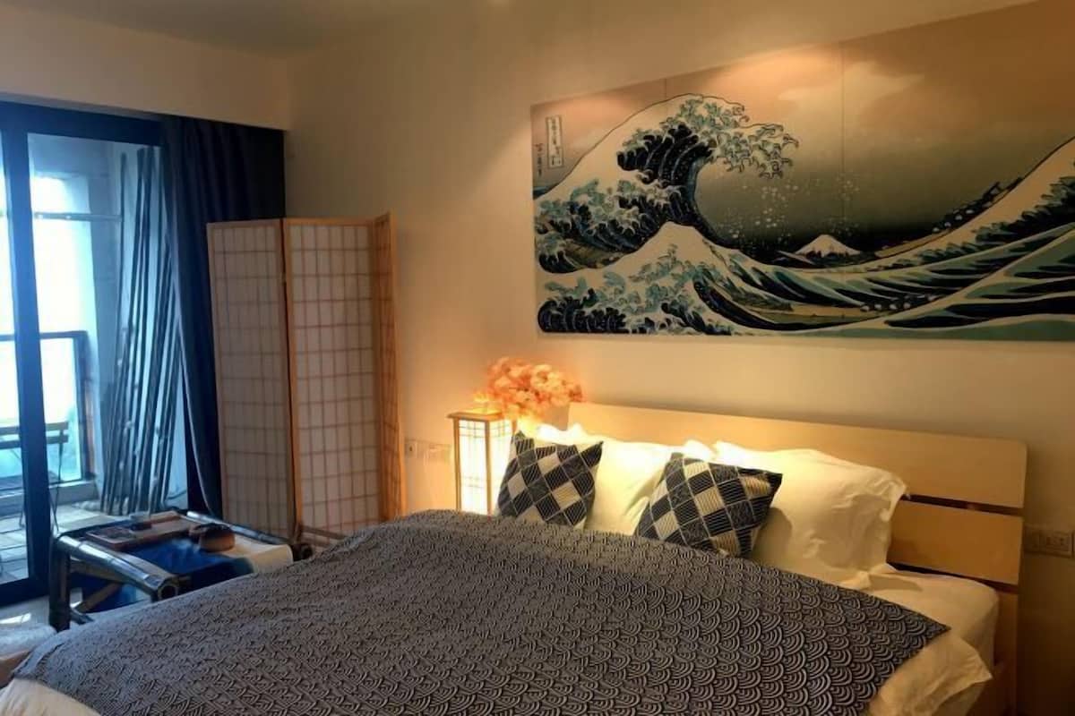 Ein Hotelzimmer mit Bett, einem großen Kunstwerk mit dem Motiv einer Welle und Blick ins Freie.
