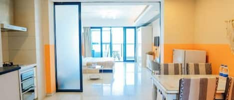 A modern hotel room with a kitchen, a dining area, and a large window providing natural light.