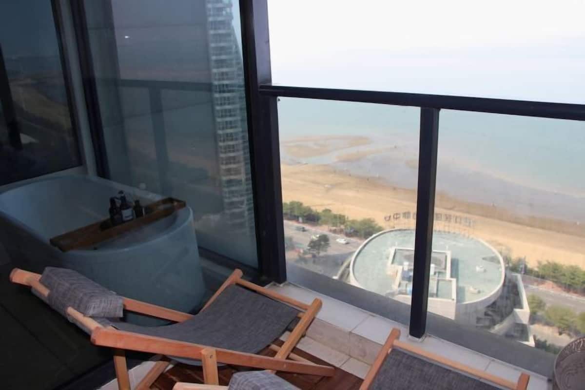 Ein Balkon mit Blick auf eine weite Landschaft, eine Badewanne und zwei Holzstühle.
