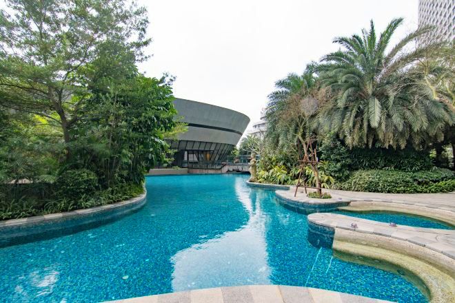 Ein Pool mit geschwungenen Rändern, umgeben von üppiger Bepflanzung und einem modernen Gebäude im Hintergrund.