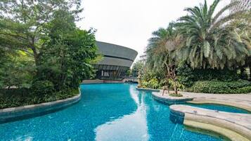 A swimming pool with curved edges, surrounded by lush greenery and a modern building in the background.