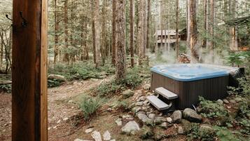 Un jacuzzi en un área boscosa con una terraza de madera y un sendero de piedra.