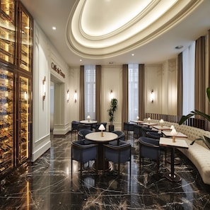 A hotel lobby with marble flooring, round tables with chairs, a sofa area, and a wine display cabinet.