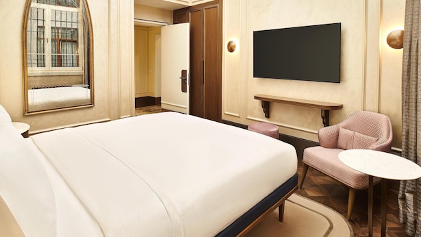 Una habitación de hotel con una cama grande, un televisor montado en la pared, una mesita redonda y una zona de estar con una silla.