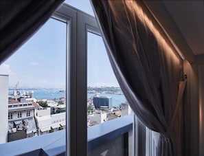 A view from a window with curtains, overlooking a cityscape with buildings and a body of water. - Les Temps Istanbul Karakoy, Curio Collection By Hilton (Istanbul)