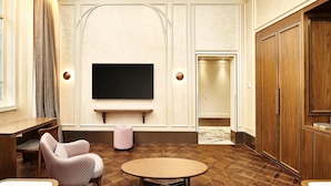 Habitación con televisión de pantalla plana montada en la pared, un armario de madera, una mesa redonda y una silla estampada.