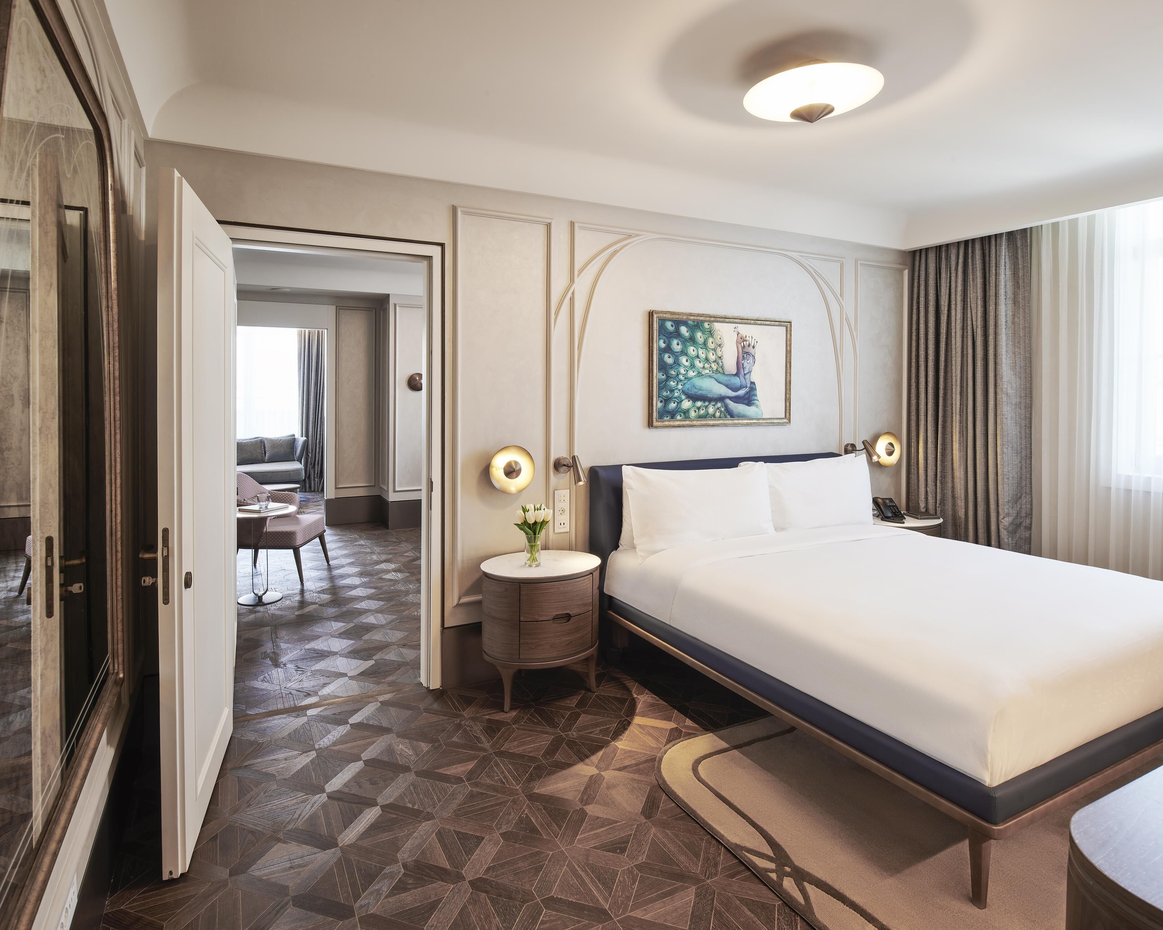 A hotel room with a bed, bedside table, lamp, and a painting on the wall.