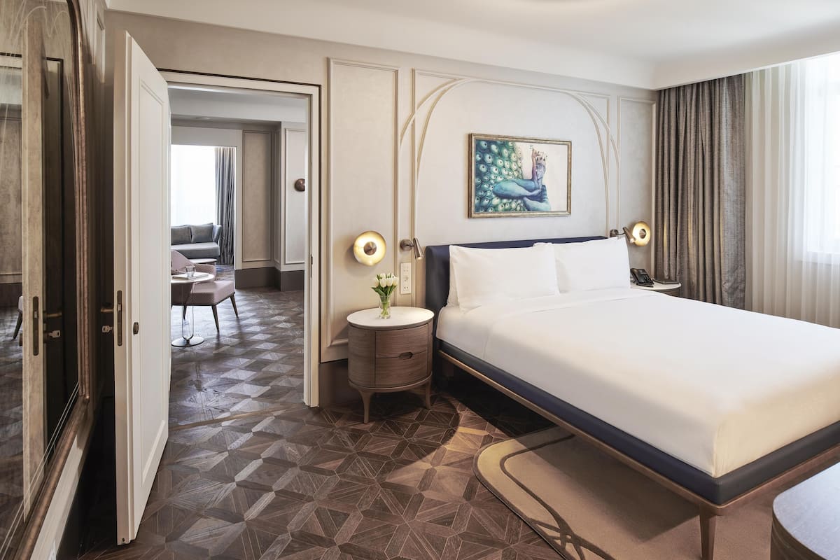 A hotel room with a bed, bedside table, lamp, and a painting on the wall.