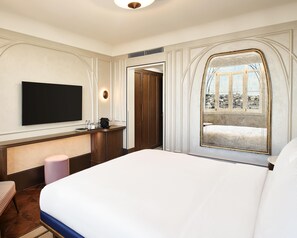 A hotel room with a large bed, a flat-screen TV mounted on the wall, a wooden desk with a coffee machine, and a window with a view of a cityscape. - Les Temps Istanbul Karakoy, Curio Collection By Hilton (Istanbul)