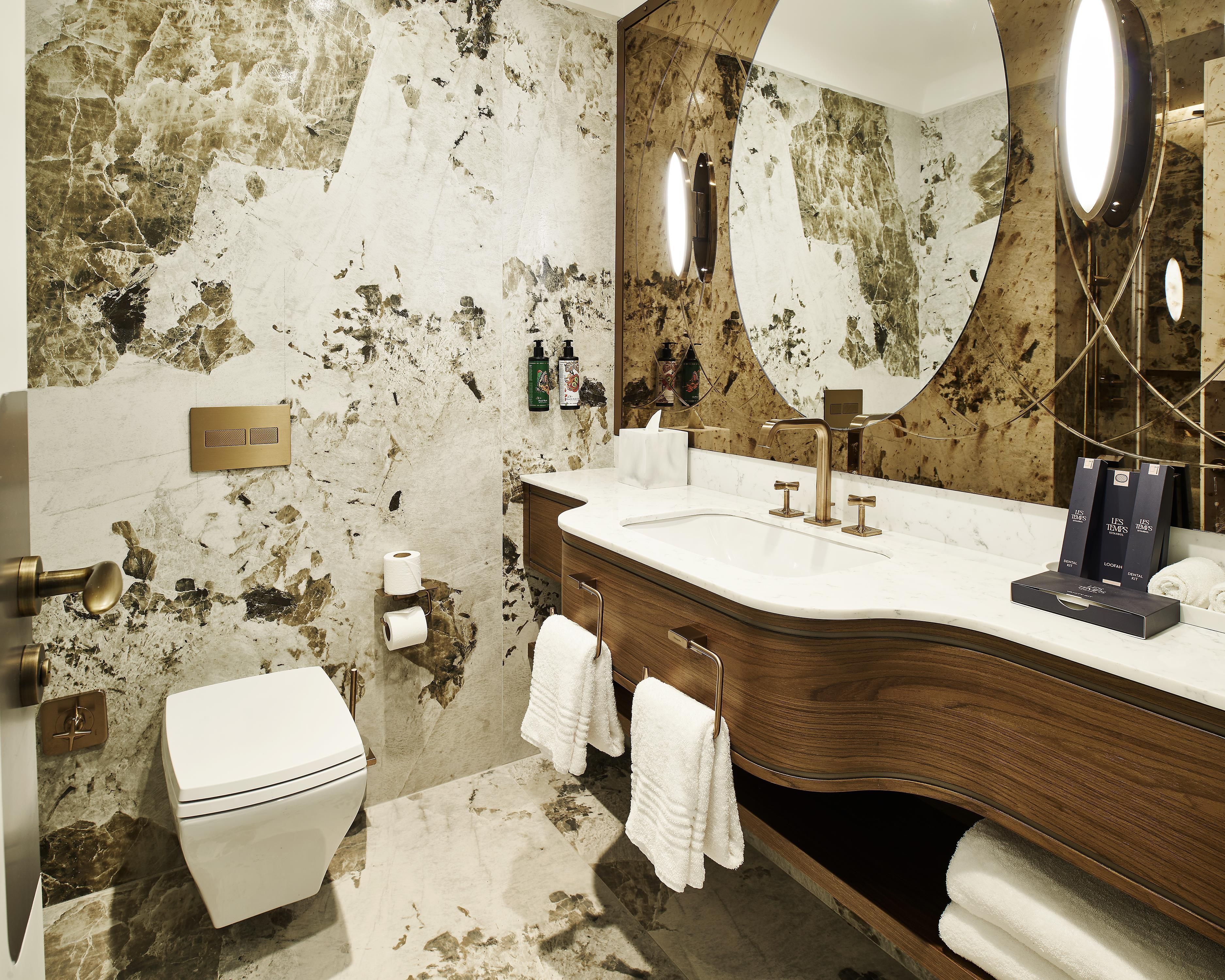 A bathroom with a marble wall, a toilet, a sink with a mirror, and a towel rack.