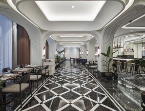 Un vestíbulo de hotel con una amplia zona de comedor, un bar y una recepción.