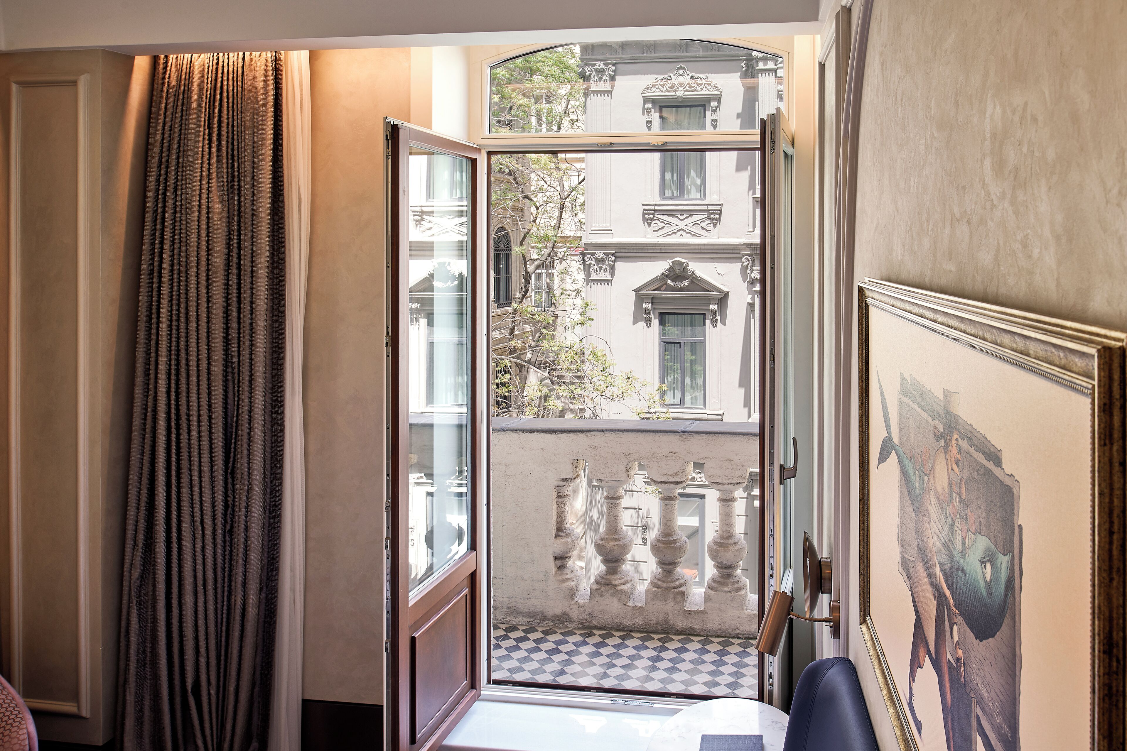 A room with a view of a courtyard, a door leading outside, and a framed artwork on the wall.