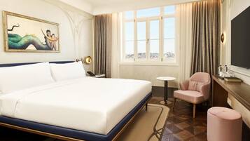 Ein Hotelzimmer mit einem großen Bett, einem Schreibtisch mit Stuhl, einem kleinen Tisch und einem großen Fenster mit Vorhängen.