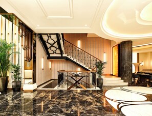 A spacious lobby with a marble floor, a staircase with a geometric railing, and a seating area with a table and chairs. - Les Temps Istanbul Karakoy, Curio Collection By Hilton (Istanbul)