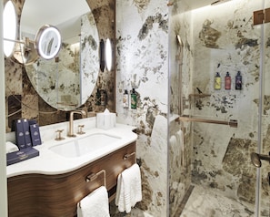A bathroom with a marble wall, a large mirror, a sink, a vanity, a towel rack, and a glass shower enclosure. - Les Temps Istanbul Karakoy, Curio Collection By Hilton (Istanbul)