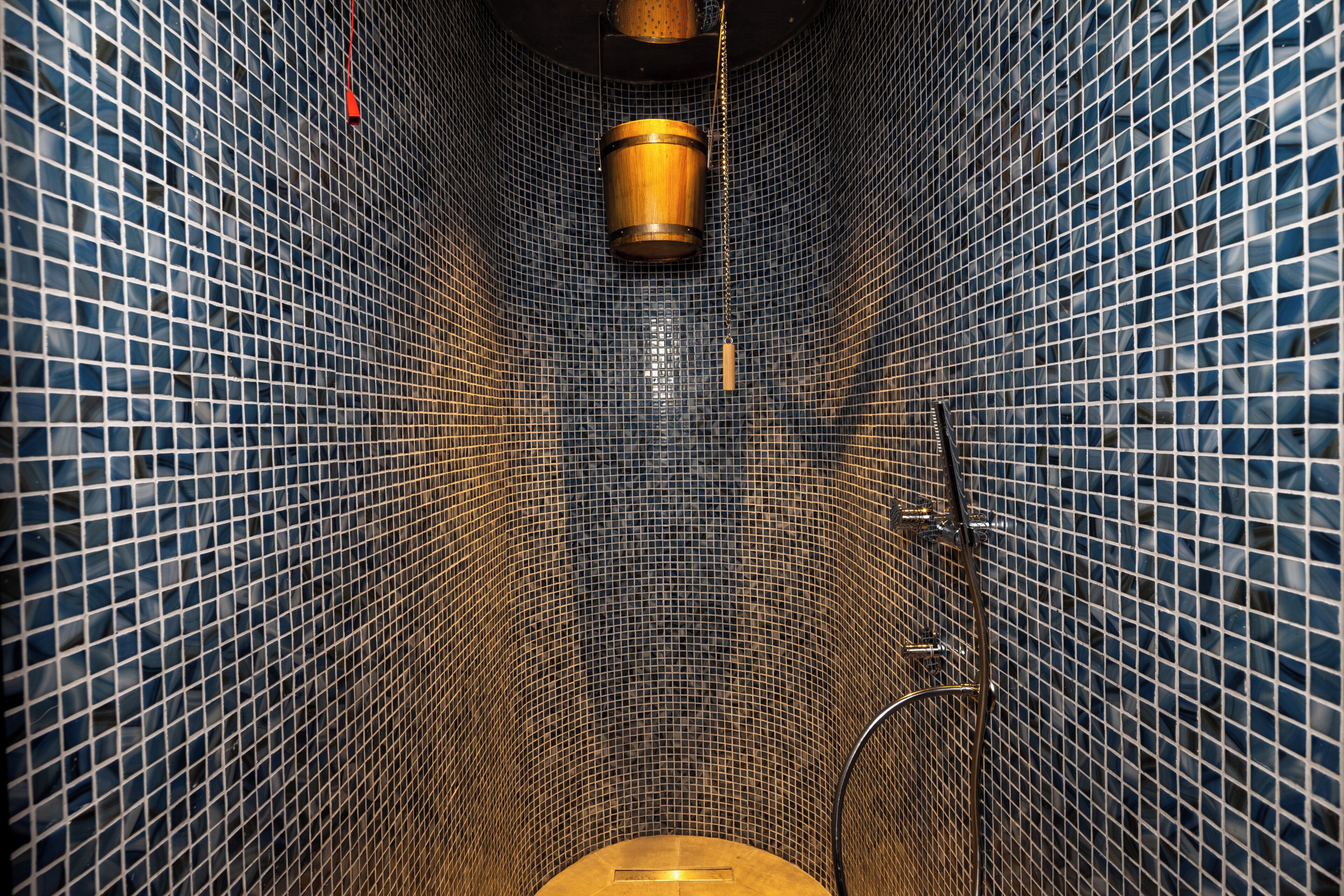 Un baño estrecho con baldosas, que incluye un inodoro, una ducha y una lámpara colgante.