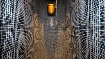 Un baño estrecho con baldosas, que incluye un inodoro, una ducha y una lámpara colgante.