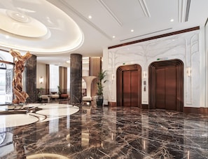 A spacious lobby with marble flooring, a central column, and two elevators.