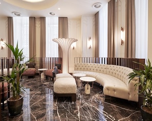 A modern hotel lobby with a curved sofa, a round coffee table, and a tall decorative pillar.