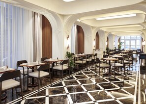 A spacious hotel dining area with multiple tables and chairs, a checkered marble floor, and large windows with curtains. - Les Temps Istanbul Karakoy, Curio Collection By Hilton (Istanbul)